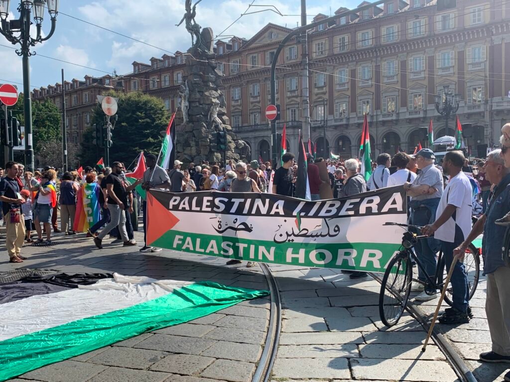 Photo of the banner heald at the front of the march, in Piazza Statuto. Banner reads "Free Palestine" in both Italian and Arabic.