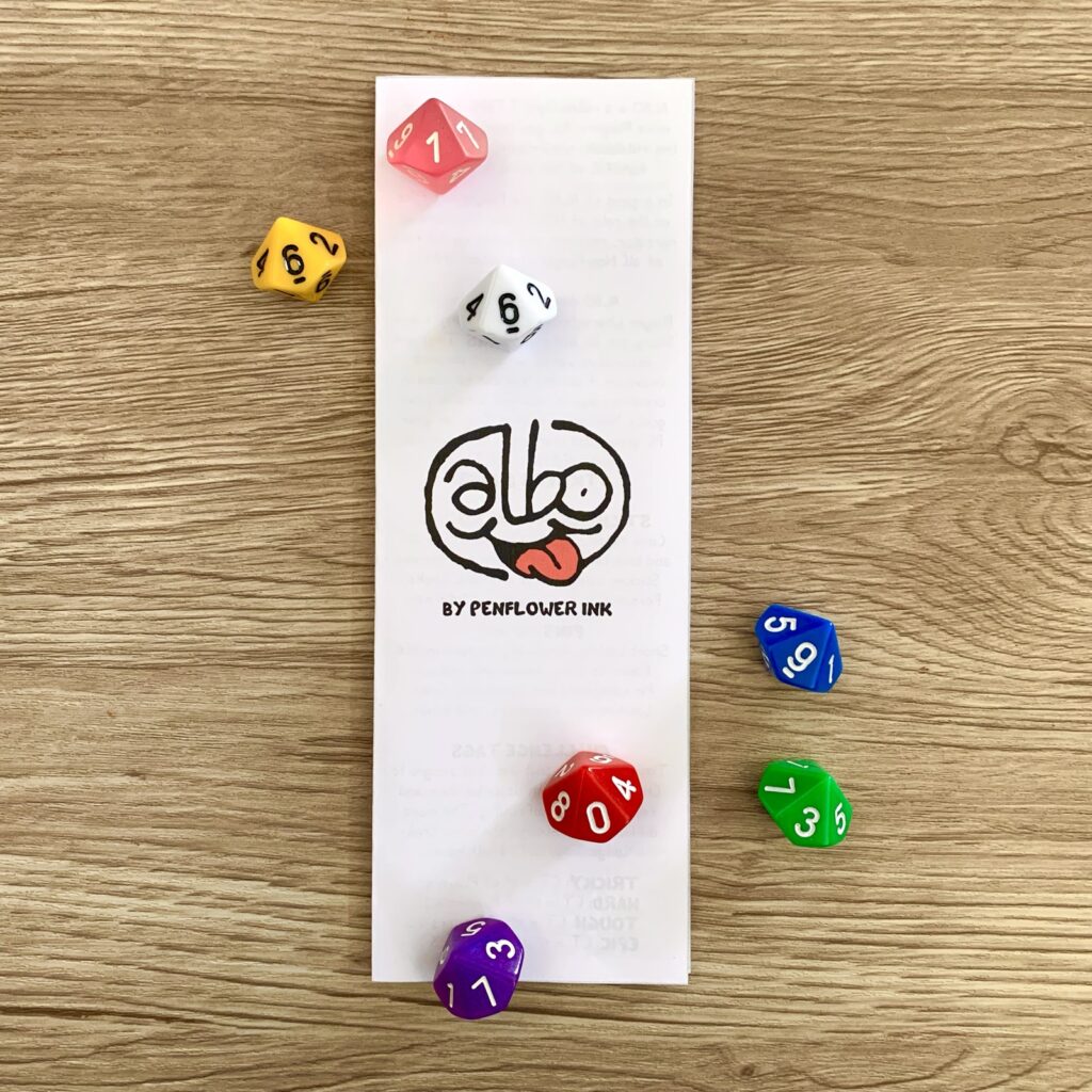 ALBO bookmark pamphlet, closed, facing cover. Colourful d10 dice for decoration.