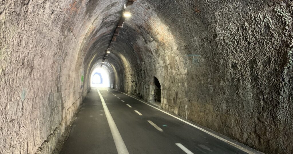 A dark, cavernous tunnel, with painting bike and pedestrian lanes and dim overhead lighting.