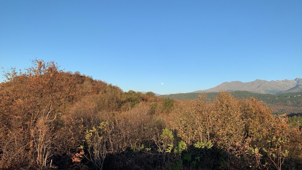 A view from the hilltop of the surrounding hills and plain under the sunrise. Full moon visible.