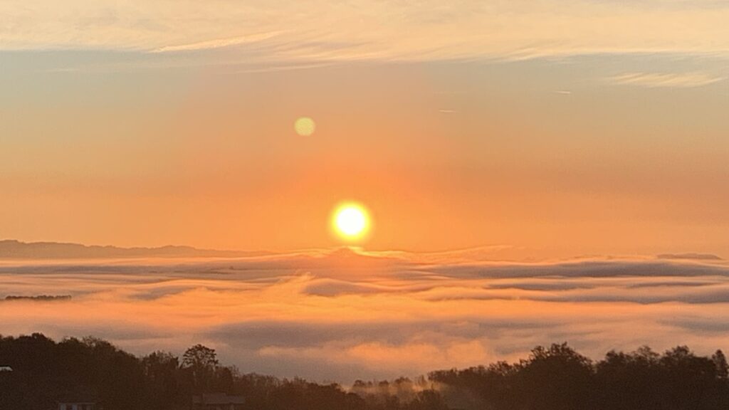 A golden sunrise from the top of the hill. The amber sun rises over a sea of fog.