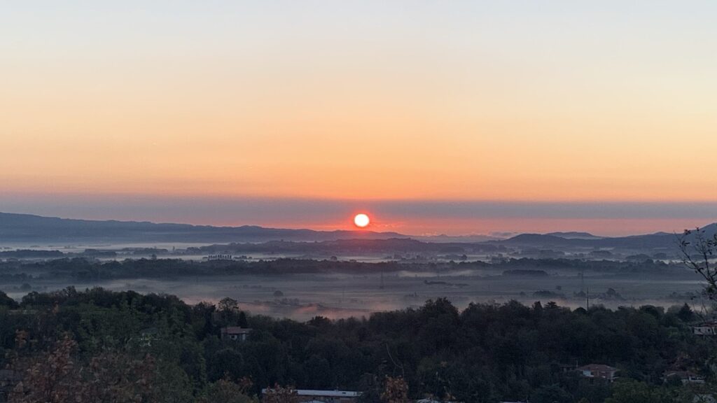 Dawn view from the top of the hill. A still red sun paints the fog a deep crimson and purple.